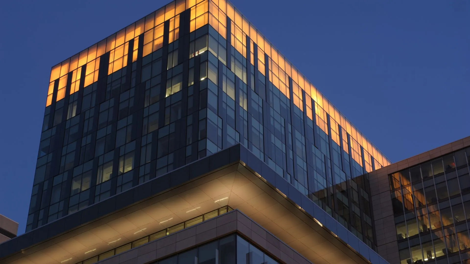 Dramatic upward view of an office tower corner with a gold-lit crown against a deep navy sky